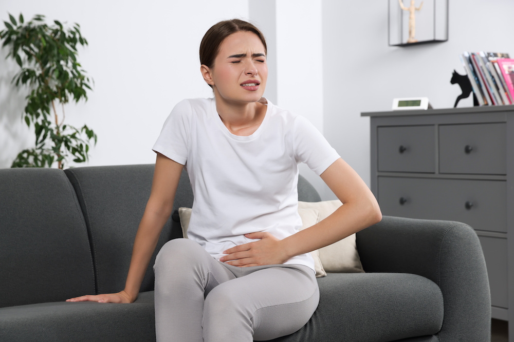 Ung kvinna som lider av urinvägsinfektion på soffan hemma